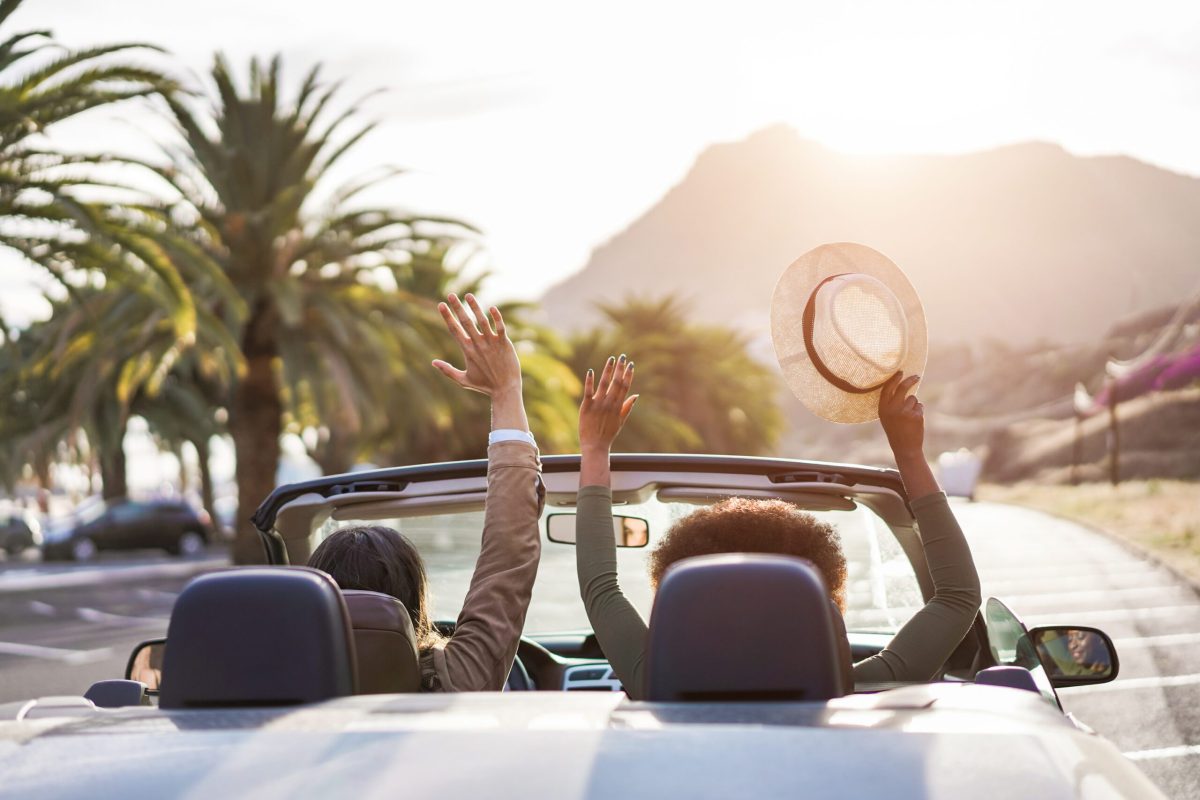 Happy people having fun in convertible car in summer vacation at sunset - Young couple enjoyng  holiday on cabriolet auto outdoor - Travel, youth lifestyle and wanderlust concept - Main focus on hat